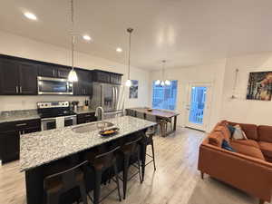 Kitchen featuring a kitchen bar, stainless steel appliances, a center island with sink, a sink, and light wood-style floors