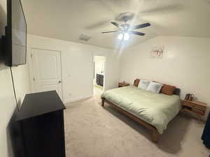 Bedroom with lofted ceiling, connected bathroom, ceiling fan, visible vents, and light carpet