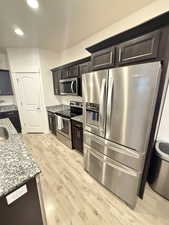Kitchen with light stone countertops, appliances with stainless steel finishes, light wood-type flooring, recessed lighting, and dark brown cabinets