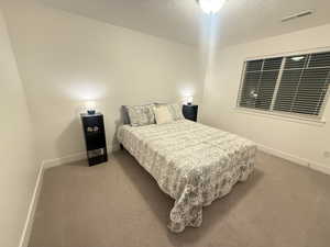 Carpeted bedroom featuring a textured ceiling, baseboards, and visible vents