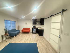 Sitting room featuring baseboards, wine cooler, a barn door, light wood-type flooring, and vaulted ceiling