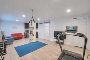 Workout room featuring a barn door, light wood-style floors, visible vents, and recessed lighting