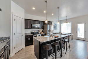 Kitchen with a sink, light wood-style floors, appliances with stainless steel finishes, light stone countertops, and a breakfast bar area