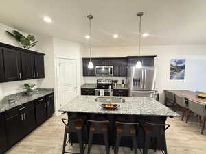 Kitchen with a sink, appliances with stainless steel finishes, light wood-style floors, and light stone counters