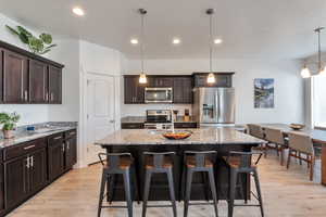 Kitchen with light wood finished floors, a kitchen breakfast bar, dark brown cabinets, and appliances with stainless steel finishes