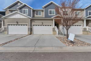 Multi unit property featuring a garage, driveway, stone siding, and stucco siding