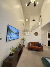 Living area with stairs, a towering ceiling, carpet, and a ceiling fan