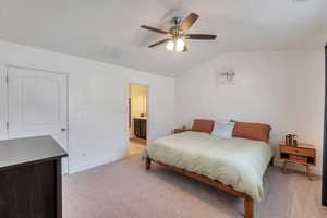 Bedroom with a ceiling fan, ensuite bathroom, baseboards, light colored carpet, and lofted ceiling