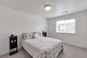 Carpeted bedroom with a textured ceiling, visible vents, and baseboards