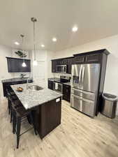 Kitchen featuring a breakfast bar, light stone countertops, stainless steel appliances, a sink, and light wood-type flooring