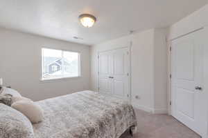 Bedroom featuring visible vents, light carpet, a closet, baseboards, and a textured ceiling