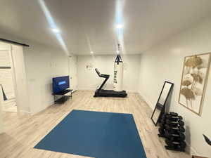 Exercise area featuring recessed lighting, baseboards, a barn door, and wood finished floors