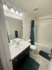 Full bathroom with toilet, vanity, a textured ceiling, visible vents, and shower / bath combination with curtain