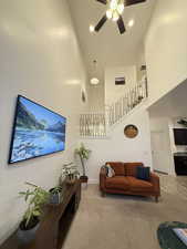 Living room featuring a high ceiling, light carpet, stairs, and ceiling fan