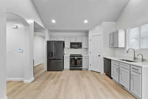 Kitchen with light countertops, lofted ceiling, a sink, arched walkways, and black appliances
