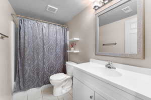 Bathroom featuring a shower with shower curtain, toilet, vanity, a textured ceiling, and visible vents