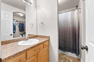 Full bathroom featuring curtained shower, a textured ceiling, a spacious closet, and vanity