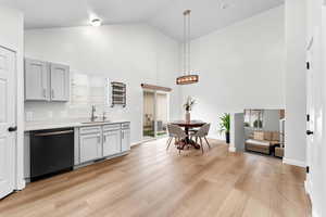 Kitchen featuring dishwasher, a sink, light countertops, light wood finished floors, and high vaulted ceiling