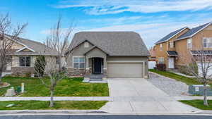 View of front of house featuring stone siding, driveway, an attached garage, a front yard, and stucco siding