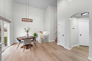 Dining area featuring arched walkways, a towering ceiling, and light wood finished floors