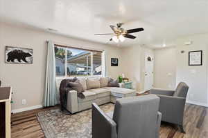 Living room with a ceiling fan, wood finished floors, baseboards, and visible vents