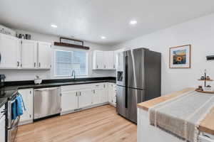 Kitchen featuring light wood-style flooring, stainless steel appliances, recessed lighting, white cabinetry, and a bar with cabinets
