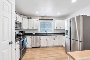 Kitchen with white cabinetry, a sink, stainless steel appliances, and dark countertops