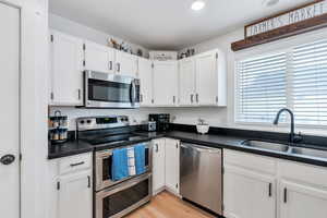 Kitchen with white cabinets, stainless steel appliances, recessed lighting, a sink, and light wood-type flooring