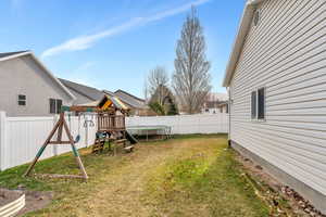 View of yard with a trampoline, a playground, and a fenced backyard