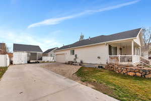 View of front facade featuring covered porch, concrete driveway, a shed, fence, and an attached garage