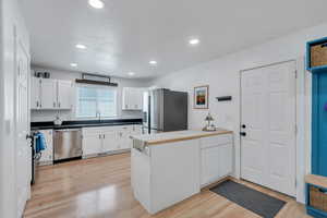 Kitchen featuring white cabinets, a sink, stainless steel appliances, a bar and light wood-style floors