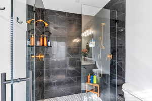 Bathroom featuring a walk in shower with seamless shower doors, tiled and golden fixtures.