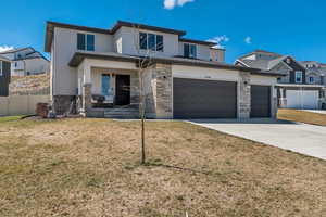 View of front of home with driveway, stone siding, a front yard, a garage, and fence