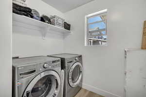 Laundry room with laundry area, washing machine and clothes dryer, baseboards, and light wood-style floors