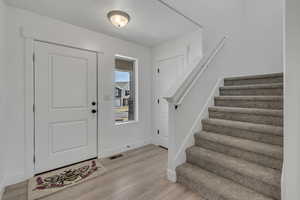 Entrance foyer with visible vents, baseboards, light wood-style floors, a textured ceiling, and stairs
