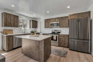 Kitchen with a center island, light countertops, light wood-style floors, appliances with stainless steel finishes, and a sink