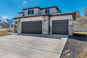 Prairie-style house featuring fence, stone siding, a garage, and concrete driveway