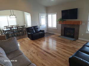 Living area featuring a tile fireplace, baseboards, wood finished floors, arched walkways, and vaulted ceiling