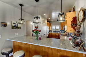 Kitchen with a peninsula, light stone countertops, appliances with stainless steel finishes, arched walkways, and brown cabinetry