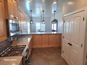 Kitchen with light brown cabinets, light stone counters, backsplash, and appliances with stainless steel finishes