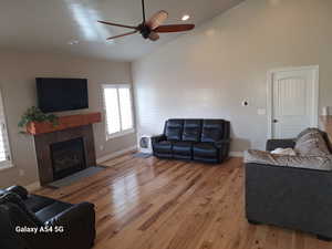 Living room with baseboards, light wood-type flooring, a fireplace, and a ceiling fan