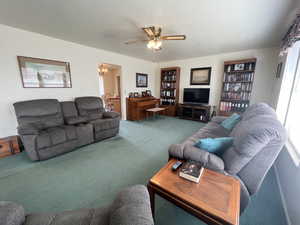 Carpeted living room with ceiling fan with notable chandelier and a textured ceiling