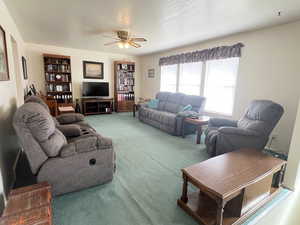 Living room with a textured ceiling, carpet flooring, and ceiling fan