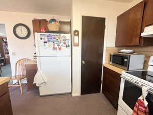 Kitchen with light countertops, carpet floors, under cabinet range hood, and white appliances