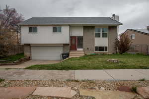 Raised ranch featuring concrete driveway, fence, an attached garage, a front lawn, and brick siding