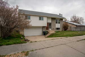 Bi-level home featuring driveway, a chimney, brick siding, a front lawn, and a garage