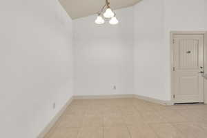 Unfurnished room featuring light tile patterned floors, baseboards, a notable chandelier, and vaulted ceiling