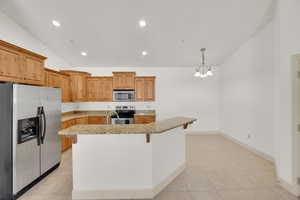 Kitchen featuring light stone countertops, an inviting chandelier, lofted ceiling, and stainless steel appliances
