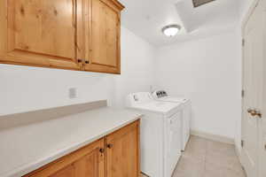 Laundry room featuring cabinet space, light tile patterned floors, baseboards, and separate washer and dryer