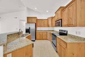 Kitchen featuring light tile patterned flooring, a sink, light stone counters, and appliances with stainless steel finishes